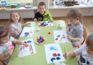 Dzieci mieszają na kartkach papieru farby w kolorach podstawowych- żółtym, czerwonym i niebieskim